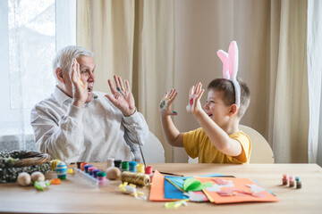 Happy elderly man granfather preparing for Easter with grandson. Portrait of smiling boy with bunny ears painted colored eggs for Easter