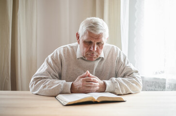 senior man praying, reading  an old Bible in his hands.