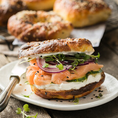 Smoked salmon bagels sandwich with soft cheese and micro greens on a cutting board.