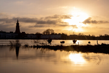 Silhouettes of trees popping up from the floodplains overflown by high water level of the river IJssel passing by Hanseatic city of Zutphen, The Netherlands, reflecting with the low sun in the surface