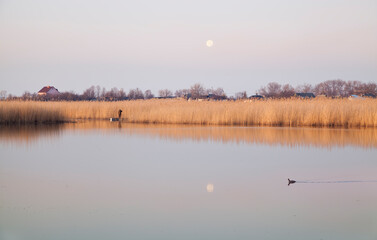 A fisheman boat on the river at sunrise, full moon reflected in the water. River Samara.