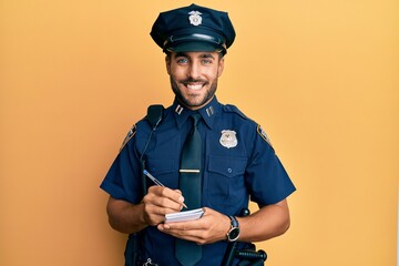 Handsome hispanic man wearing police uniform writing traffic fine smiling with a happy and cool...