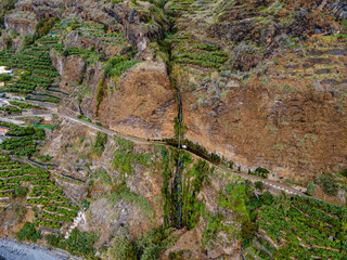 A car drives under Ponta do Sol waterfall on the coast of Madeira Island - waterfall falls on a road