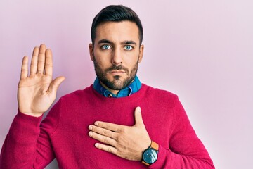 Young hispanic man wearing casual clothes swearing with hand on chest and open palm, making a...