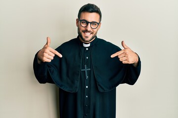 Young hispanic man wearing priest uniform standing over white background looking confident with...