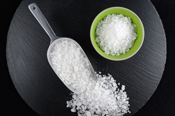 Small porcelain bowl  and scoop full of sea salt on black dish