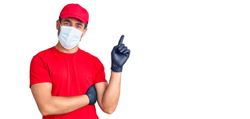 Young hispanic man wearing covid-19 safety mask smiling happy pointing with hand and finger to the side