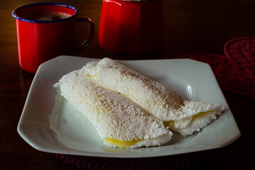 Duas tapiocas recheadas dentro de um prato branco e uma xícara vermelha com café.