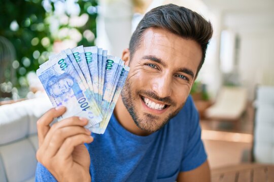 Young hispanic man smiling happy holding south african rands banknotes at the terrace.