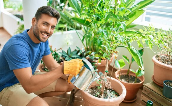 Young handsome man smiling happy caring plants using watering can at terrace