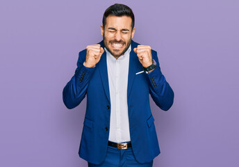 Young hispanic man wearing business jacket excited for success with arms raised and eyes closed celebrating victory smiling. winner concept.