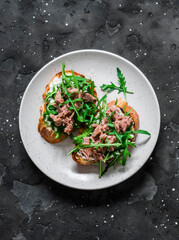 Snack sandwiches with canned tuna, cream cheese and arugula on a dark background, top view
