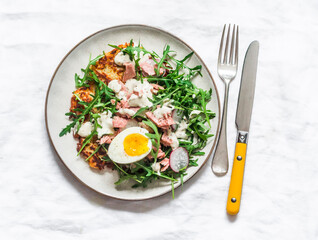 Potato latkes and salad with arugula, canned tuna, boiled egg, yogurt, mustard dressing on a light background, top view
