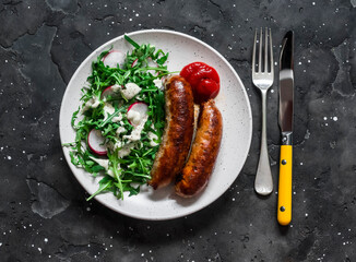 Fried pork sausages and salad with arugula, radish and mustard, yogurt dressing on a dark background, top view