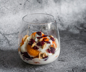 Natural greek yogurt with tangerine, dried cranberries and nuts on a grey background, top view