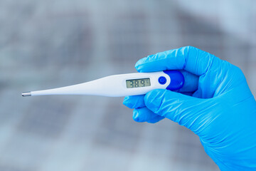 Hand in blue glove holding a digital thermometer on white background. Medical worker wearing...