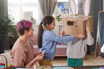 Family of three making rabbit costume from cardboard box they preparing for Easter holiday