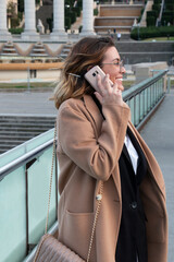 Young blonde woman with glasses laughs talking on the mobile in the city