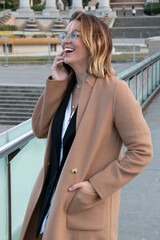 Young blonde woman with glasses laughs talking on the mobile in the city