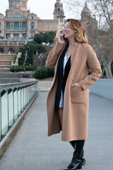 Young blonde woman with glasses laughs talking on the mobile in the city