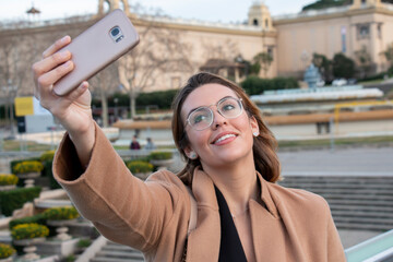 Young blonde woman with glasses takes selfie in the city