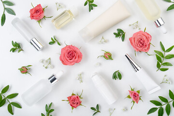 Obraz na płótnie Canvas Flat lay cosmetic bottles and containers with pink roses and green leaves background on white table