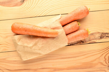 Several juicy natural, unpeeled carrots in a paper bag on a wooden table, close-up, top view.