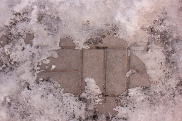 Melting snow on the paving slabs during spring thaw. Patch of sidewalk in thawing snow. Sunny day. 
