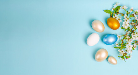 Easter painted mother-of-pearl eggs with cherry blossoms on a blue background with copy space. Seasonality concept, spring, postcard, holiday. Flat lay, place for text. View from above