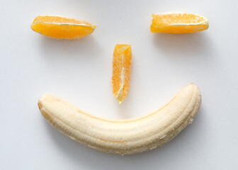 Cheerful smiley face with peeled banana and orange slices on a white background.