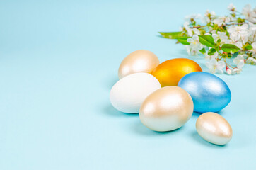 Pearl colored eggs for Easter with branches of blossoming cherry on a blue background with copy space. Seasonality concept, spring, postcard, holiday. Flat lay, place for text. Close-up.