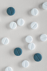 White and blue pills lie on gray paper. Close up. Light vertical background or backdrop on the theme of medicine, health care, drugs, pharmacology. Tablets of different colors. View from above. Macro