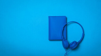 Notebook and headphones with a wire in a blue background.