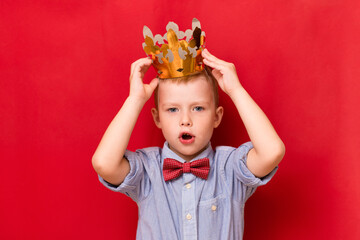 Cute child boy puts golden crown on your head on red background