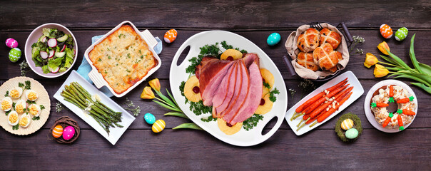 Classic Easter ham dinner. Top view table scene on a dark wood banner background. Ham, scalloped...