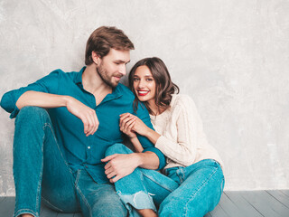 Smiling beautiful woman and her handsome boyfriend. Happy cheerful family sitting in studio on the floor near gray wall.Valentine's Day. Models hugging. Concept of love