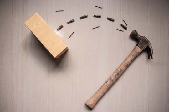 hammer throwing nails and screws into a wooden plank creating an arc on a beige background, with shooting effect and tethering on an inclined surface. Types of tools for work at home.