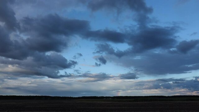 Beveled plowing field by summertime under dramatic cloudy sky with rainbow at sunset time, beautiful nature rural landscape. Time lapse video, 4k.