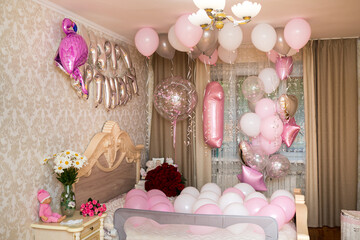 The room is decorated for the birthday with balloons and flowers in pink shades.
