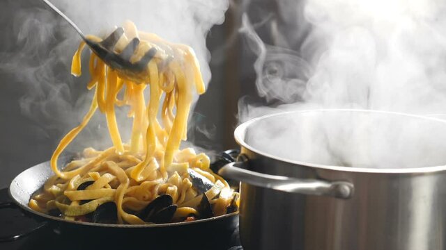 Chef serving pasta on plate. Close up. Putting pasta in plate with kitchen tongues and laddle. Italian cuisine. White steam rising in slow motion. Vapour or White steam rising up on black. Full hd