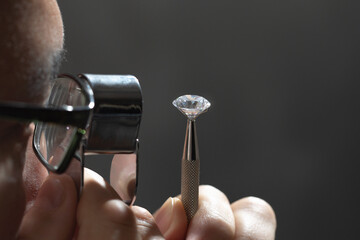 Close up of asian male diamond dealer buyer expert evaluates polished diamonds at exhibition. High quality photo