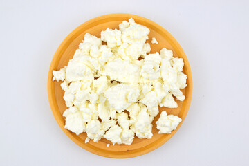 Fat crumbly cottage cheese on wooden platter isolated on white background