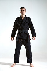 Frowning guy in black kimono fighter posing on white studio background with copy space, mix fight...