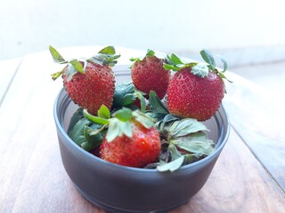 Red strawberries with gree  leaves in a bowl placed on wodde  stool