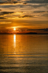 Vertical photo of Sunset over Umea river Mountains, summer sky with clouds highlighted by orange red Sun. Sunlight path on water Storuman, Lapland, Sweden