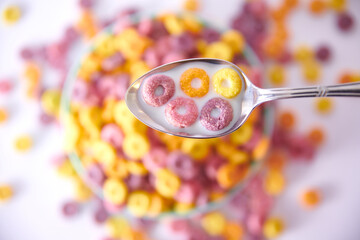 Top view of a spoon with multicolored fruity cereals and milk on a blurred background