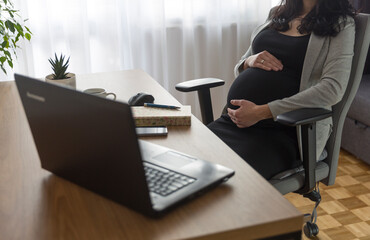 Pregnant woman is working on computer laptop and mobile phone, business. Being pregnant at work. ...