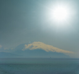 alone mount top in dense clouds above sea bay under a sparkle sun, natural sea background