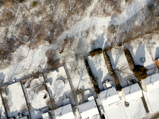Aerial drone view of roads and houses winter landscape. Winter city streets from a bird eye view. Top perspective of  snow covered buildings. Roads, lawns, cars and trees covered with snow from above.