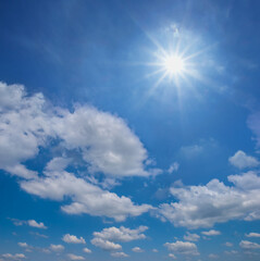 sparkle sun among cumulus clouds, blue summer sky background